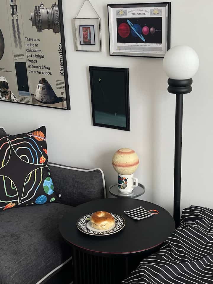 Monotone living room featuring a black sofa, side table with bagel and wall art, complemented by a floor lamp creating a cozy atmosphere