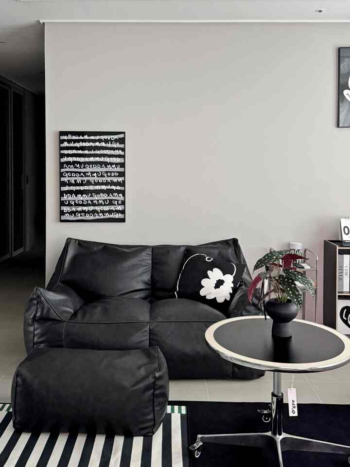 ホワイトの壁に囲まれたブラックレザーのビーンバッグソファとサイドテーブル、パターンラグが配置されたモダンでミニマルなリビングルーム