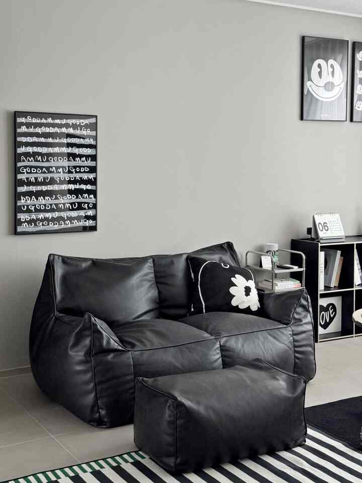 ブラックとグレーのモノトーンのリビング、黒いビーンバッグソファとスツール、本棚やサイドテーブルが配置されたモダンなインテリア