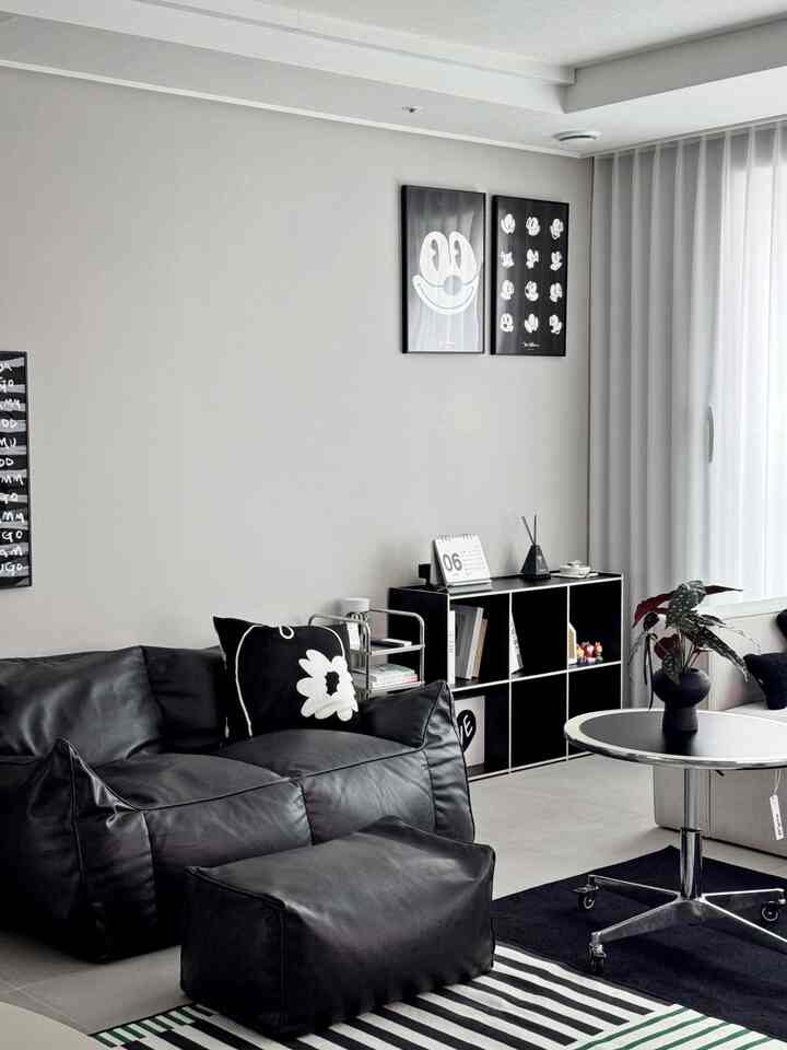 Modern living room in black and white tones featuring bean bag sofa and stool, bookshelf, and round coffee table with a clean aesthetic