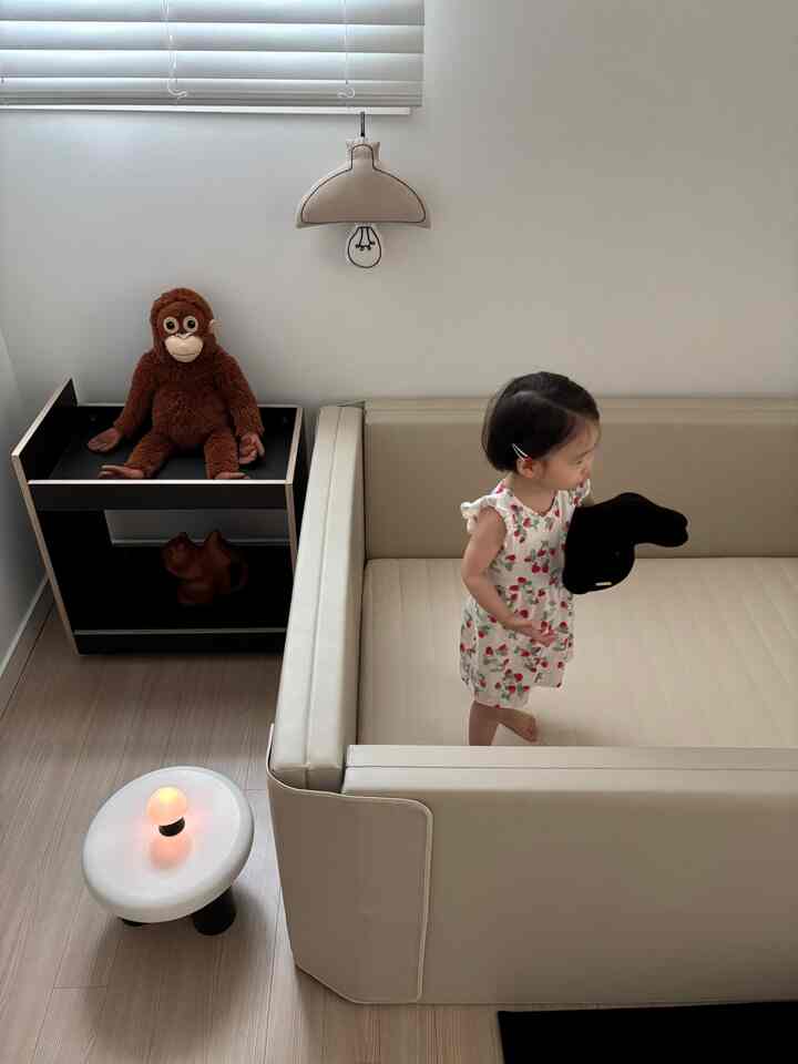 ベージュとクリーム色調の子供部屋、中央に子供がいるクリーム色のソファベッドが配置されたミニマルな空間