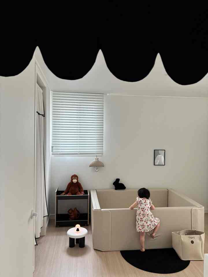 ナチュラルカラーの子供部屋、ベージュのベビー柵と木目調の床、白いブラインド、黒いラグが配置された雰囲気のあるインテリア