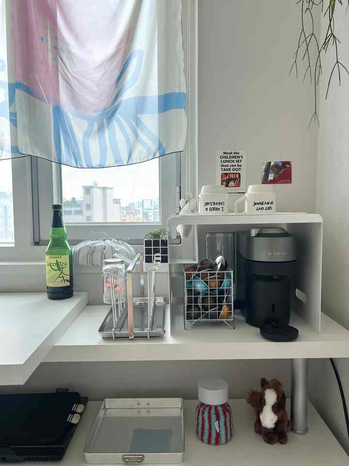 白を基調とした小さなおうちカフェ、コーヒーマシンとカプセル、トレイが整理されたモダンな収納ラックのある清潔感のある空間