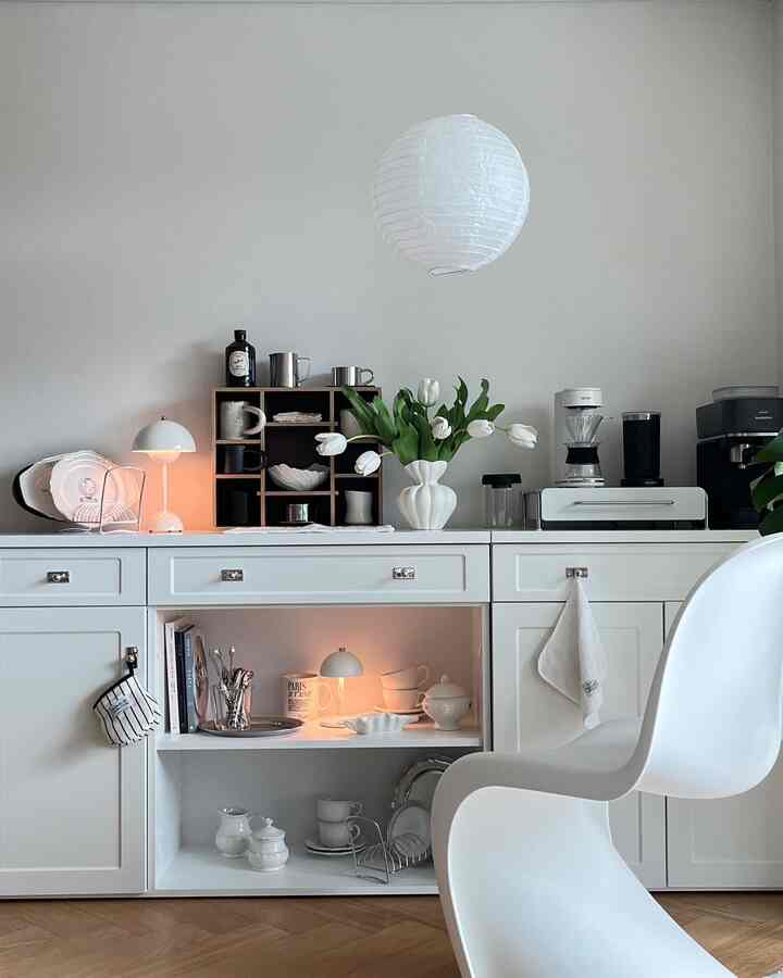 ホワイトトーンのキッチン、シンプルな家具とコーヒーマシン、花瓶、照明が配置されたおうちカフェの雰囲気あるインテリア