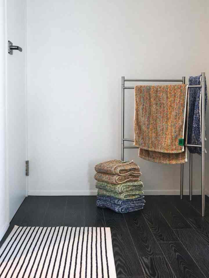Modern, clean bathroom with white walls and dark wood floor, featuring a stainless steel towel rack holding multicolored towels neatly organized