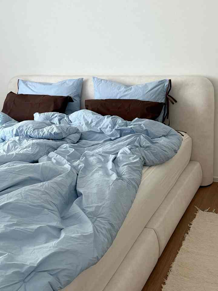 A modern bedroom featuring a soft beige bed frame and blue duvet cover creating a calm atmosphere