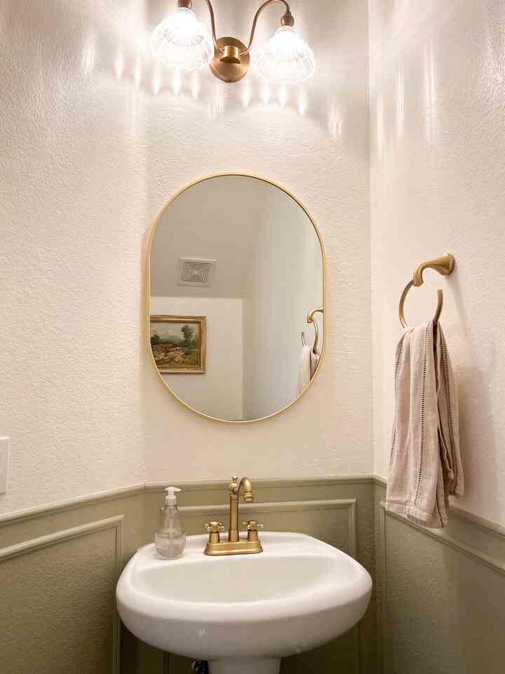 White and gold toned bathroom powder room featuring a gold-framed oval mirror, antique brass faucet, and matching wall sconces in a neat setup