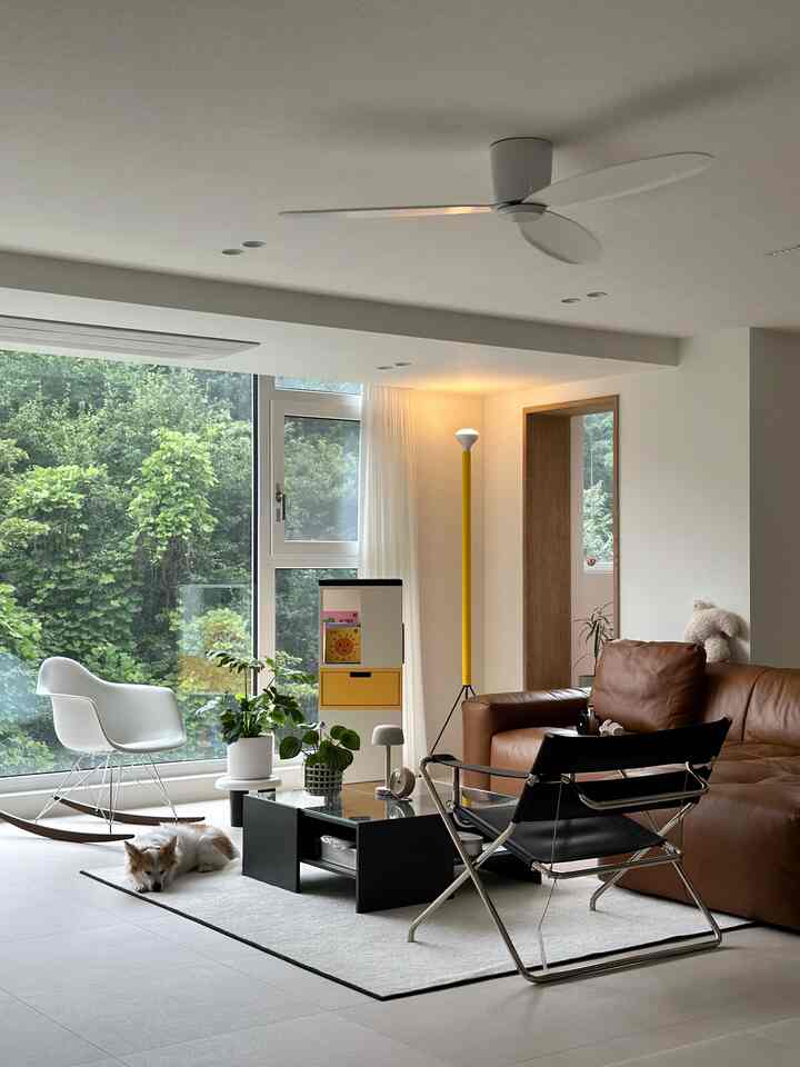 ナチュラルな色調のリビング、ブラウンレザーのソファとロッキングチェア、回転式本棚が配置されたモダンなインテリア