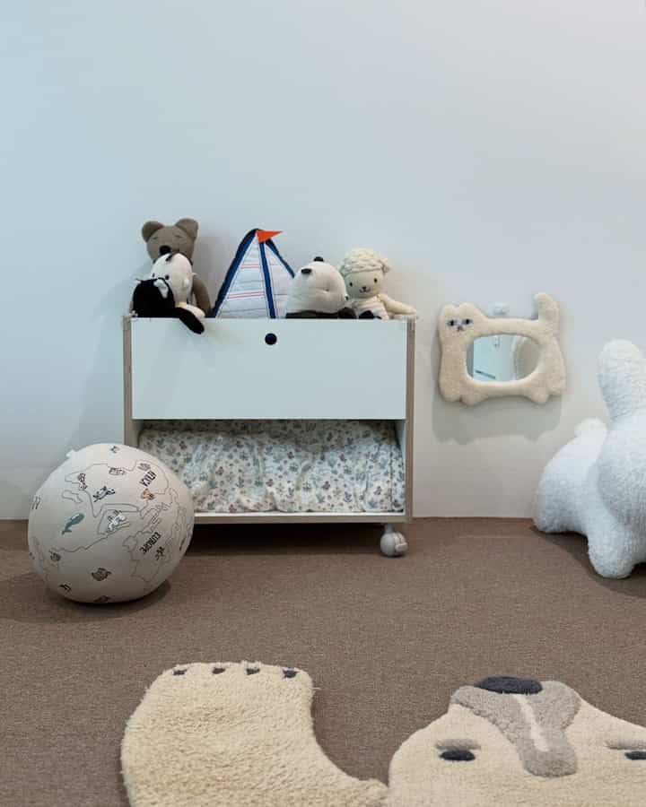 ベージュの床と白い壁、中央に赤ちゃん用のブックカートとぬいぐるみが配置されたベビールームのインテリア