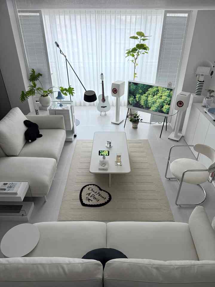 Modern living room in white tones with white leather sofa, coffee table, and plants creating bright and clean atmosphere