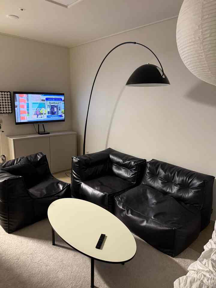 白い壁と天井が広がるモダンなリビング、中央と右側に黒のビーンバッグソファとアーチ状のフロアランプが配置された印象的な空間