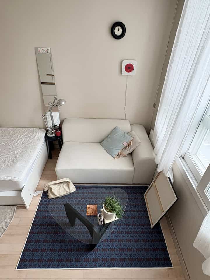 A white and blue toned studio living room featuring a simple sofa with cushions and a glass coffee table, creating a natural and minimal atmosphere
