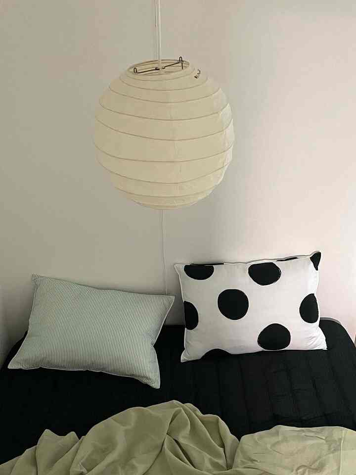 Black and white toned bedroom featuring a black bed, polka dot pillows, and a round pendant light creating a clean atmosphere