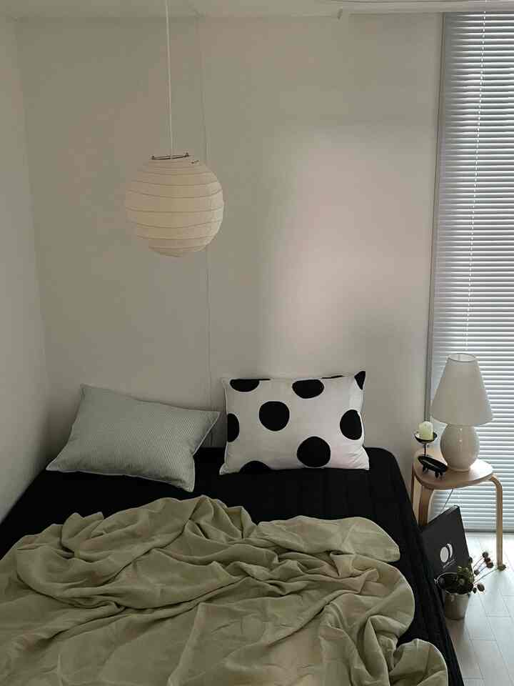 Simple bedroom in white and black tones featuring a pendant light, blinds, and minimal bedding in a small space