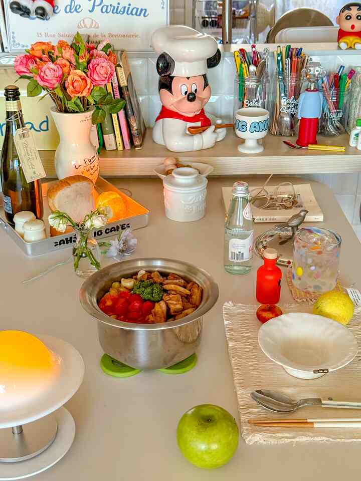 明るいグリーンとベージュの色調のキッチンテーブルに花瓶やカトラリー、料理が配置されたナチュラルでモダンな雰囲気のインテリア