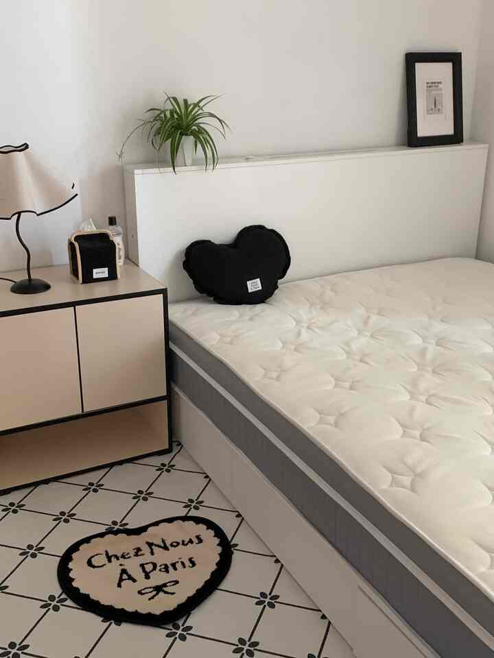 White and black toned bedroom featuring a bed with mattress and a storage cabinet, creating a clean space