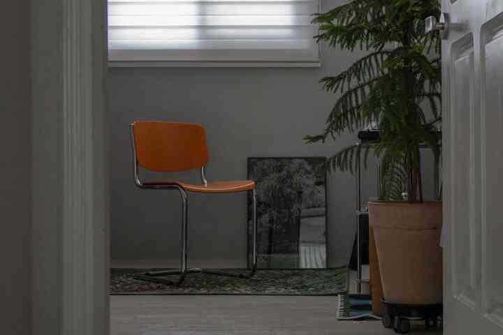 グレーの壁とナチュラルトーンのコンパクトな部屋、ミッドセンチュリーモダンの椅子と緑の植物が配置された落ち着いたリラクゼーションスペース