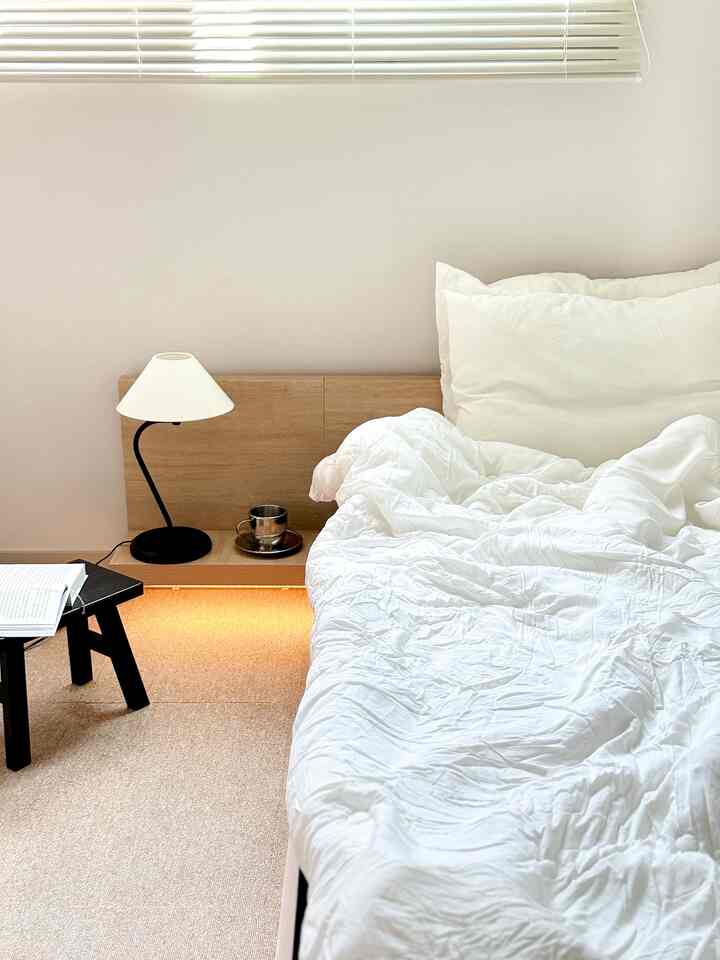 ホワイトと木目調が調和した寝室、シンプルなベッドフレームとナイトテーブルが配置された落ち着いた空間