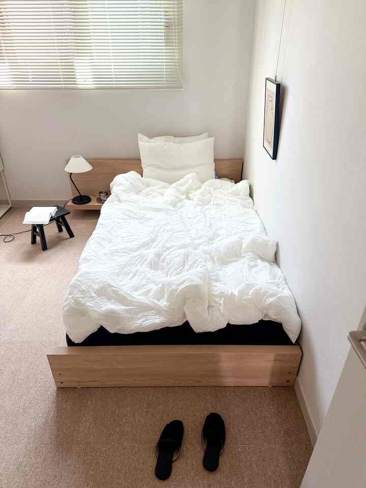 Small bedroom space featuring a low wood-tone bed with white bedding and minimal black accents
