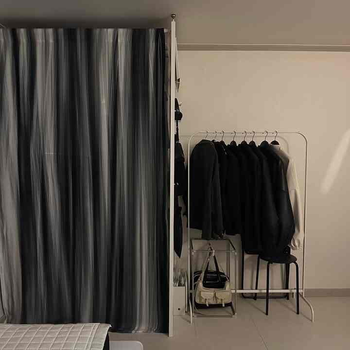 白い壁と床のミニマルな空間に、ハンガーラックとパンチングパーティション、カーテンで仕切られた実用的なクローゼット空間