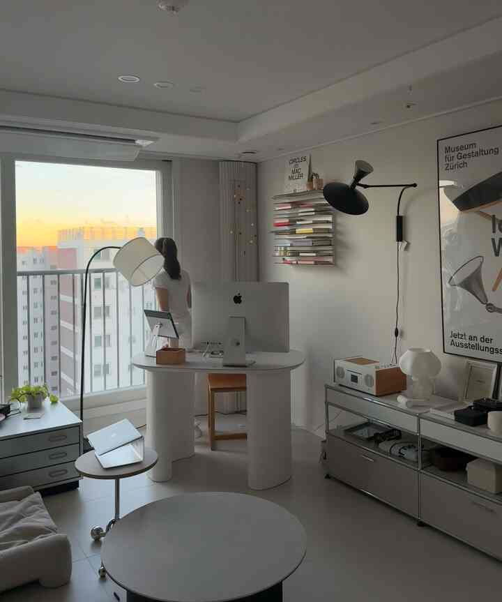 ホワイトトーンのホームオフィス、中央に机とモニター、棚や照明が配置されたモダンな印象的な空間