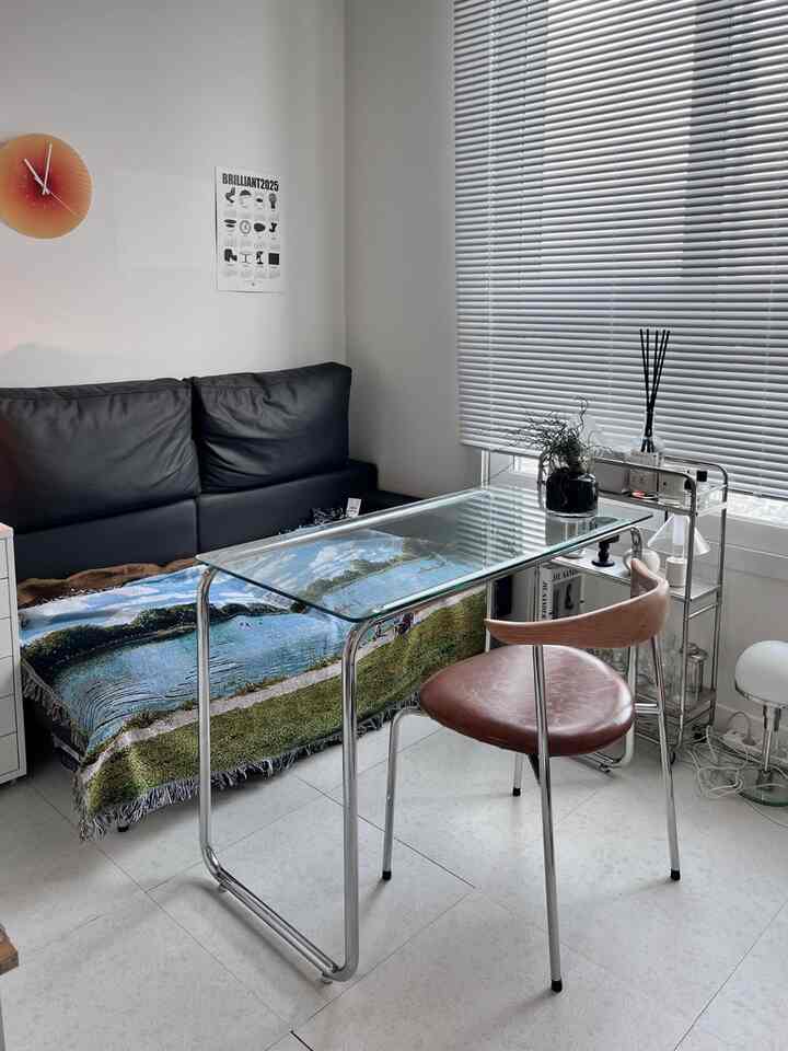 ライトグレーのトーンのワンルームリビング、ブラックソファと透明なガラステーブルが配置されたミニマルな空間