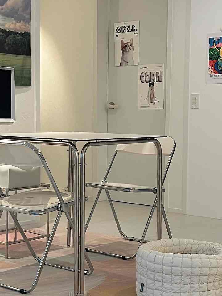 白を基調としたリビング、ステンレス製のダイニングテーブルと透明な折りたたみ椅子が配置されたミニマルで清潔感のあるインテリア