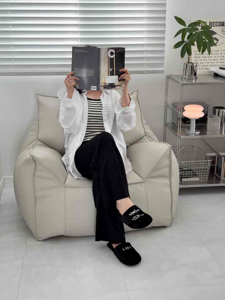 ベージュのビーズクッションと白いブラインドがあるシンプルでモダンなリビング、ホームシューズを履いて本を読む人がいる