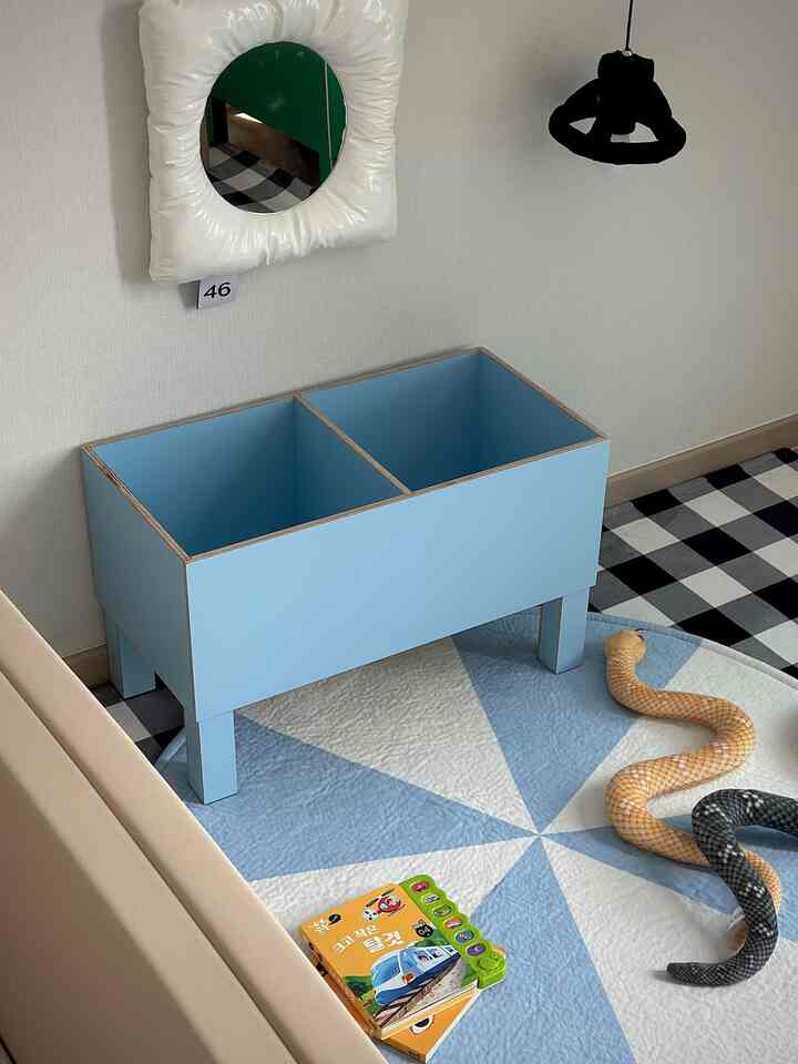 青い収納ボックスとベージュのソファが置かれた子供部屋、床にはおもちゃと北欧風のカーペットが敷かれた雰囲気のあるインテリア