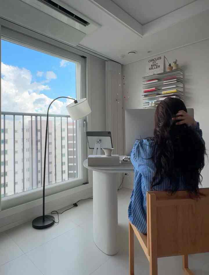 ホワイトとネイビートーンのコンパクトなワンルーム、モダンな印象のホームオフィスで、机とフロアランプが配置されたインテリア