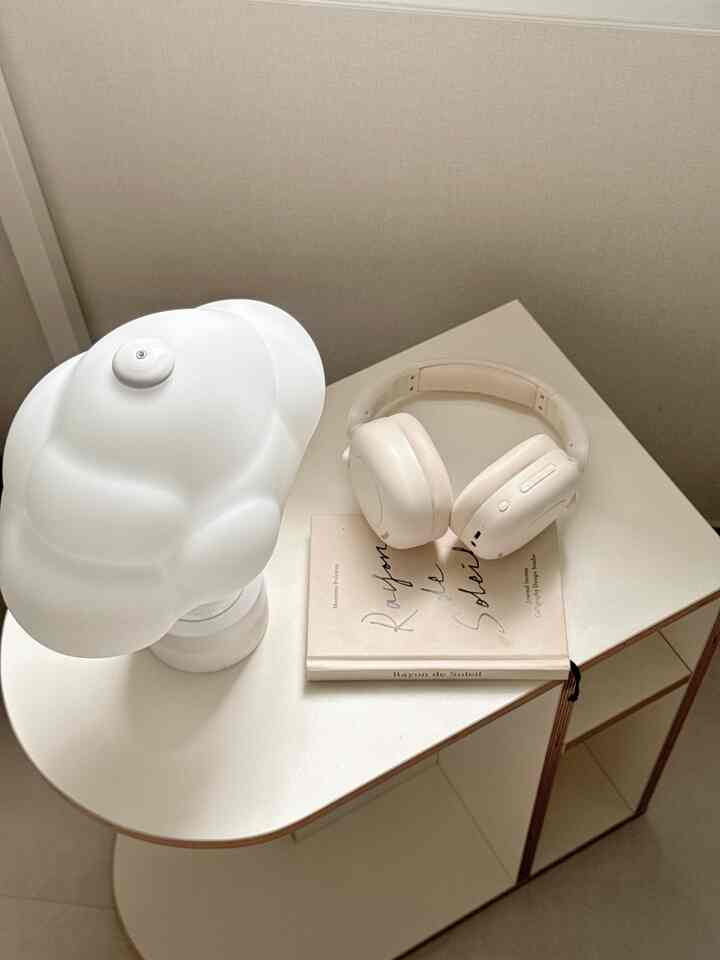 ホワイトトーンでミニマルな寝室、サイドテーブルに個性的な照明とヘッドホンが配置された印象的なインテリア