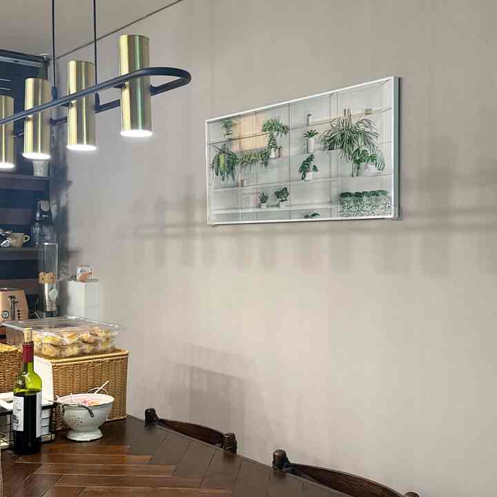 ブラウンの木製ダイニングテーブルと壁に掛けられた緑の植物の絵が調和したナチュラルなキッチンダイニングスペース