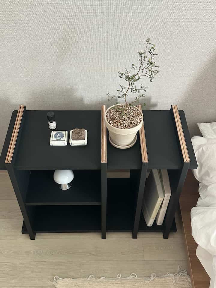 A simple and modern bedroom featuring a black nightstand bookshelf on natural wood flooring