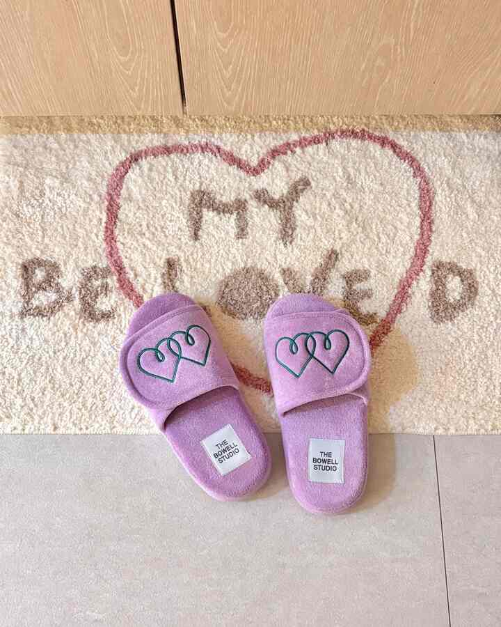 Entrance space with light gray tile floor and beige bath mat featuring purple indoor slippers placed centrally