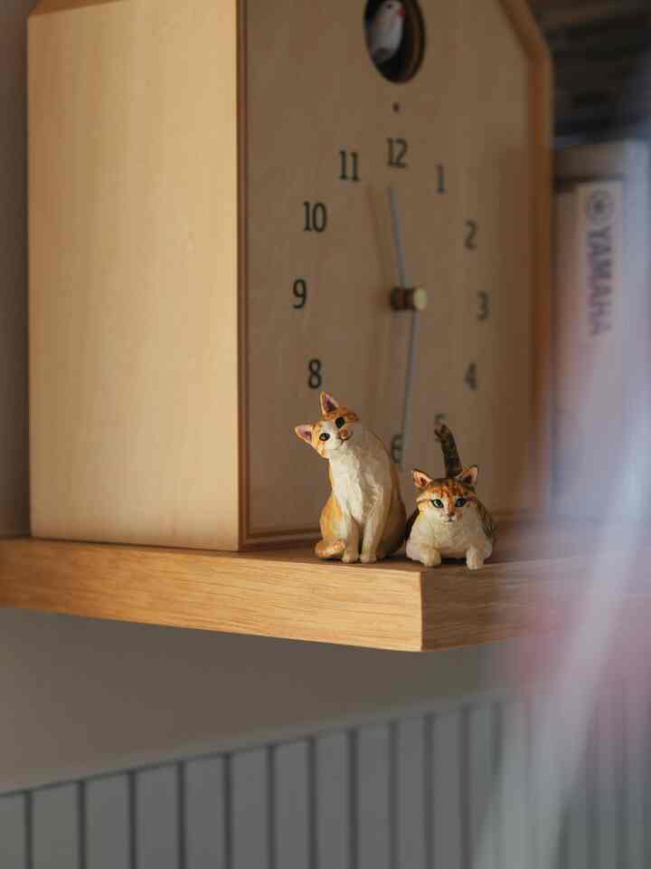 Natural wood tone wall shelf featuring a birdhouse-style clock and two cat figurines in a minimalistic setting