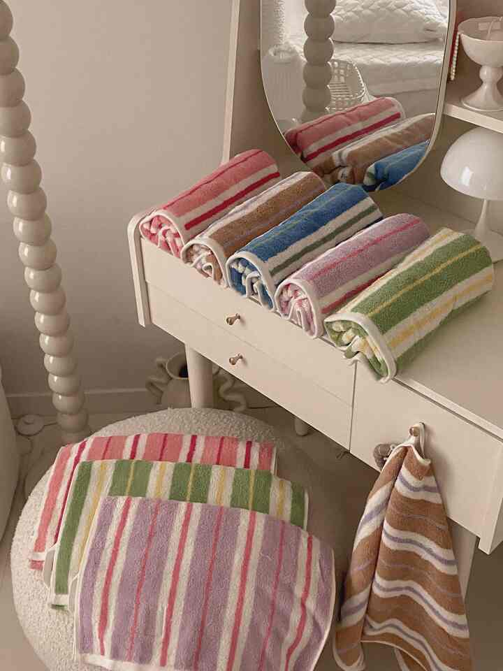 ベージュとアイボリーのトーンのウォークインクローゼット兼パウダールーム、ストライプのタオルとスツールが整然としたシンプルなインテリア