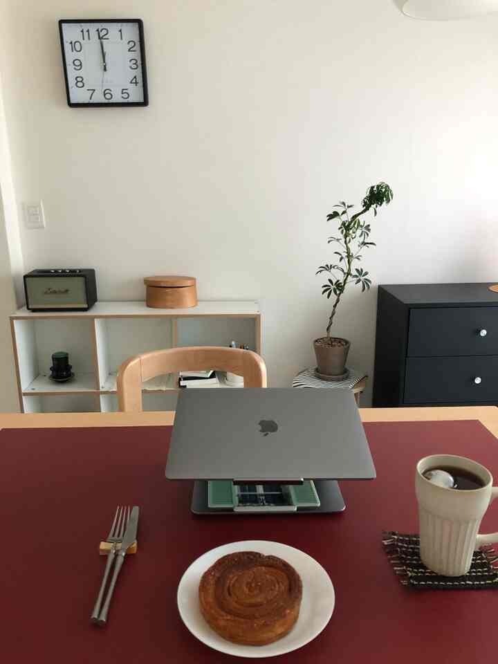 白い壁と木目調の家具が配置されたミニマルなダイニングルーム、テーブル上にノートパソコンと食器が並び、落ち着いた作業空間を演出