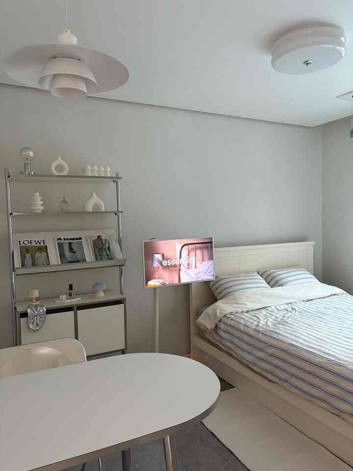 白とグレーのトーンが支配するワンルームの寝室、中央にシンプルなダイニングテーブルとミッドセンチュリーモダンの家具が配置された清潔感のあるインテリア