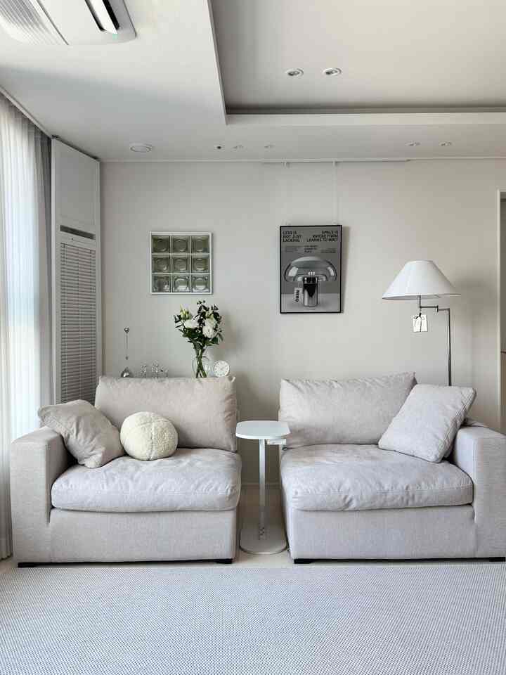 ホワイトとベージュの色調のリビング、シンプルなソファと照明ポスターが配置されたミニマルで洗練されたインテリア