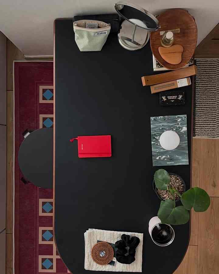 ナチュラルなトーンのコンパクトなダイニング、黒いダイニングテーブル、木製のテーブルクロス、植物と卓上鏡が配置された雰囲気のあるインテリア