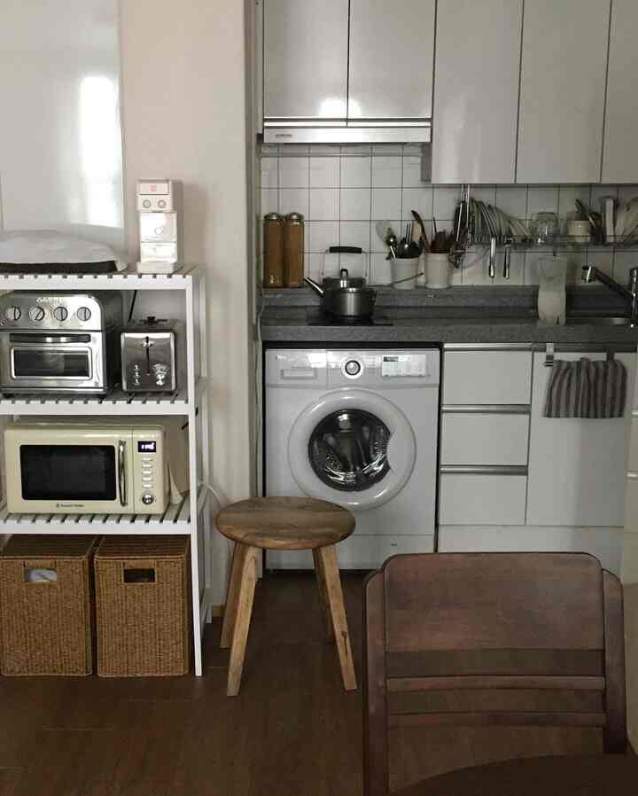 白を基調としたキッチンに木製のスツールやバスケット、レトロな家電が配置された落ち着いたワンルームのキッチンスペース