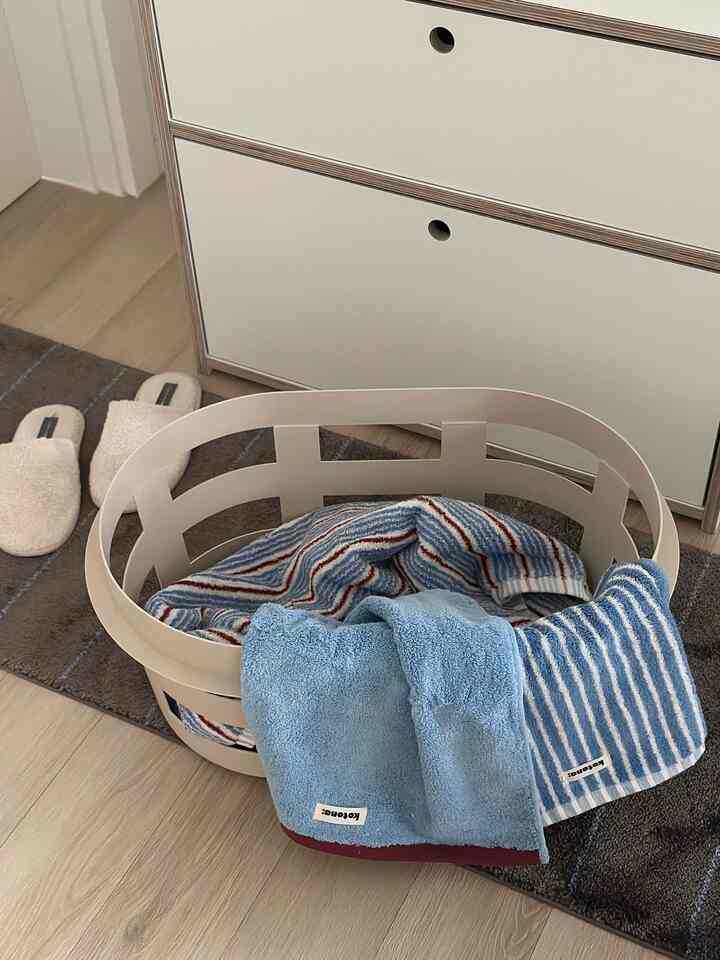 Bathroom space with brown wood-toned floor and white storage, featuring a basket with various towels and bathroom slippers arranged neatly