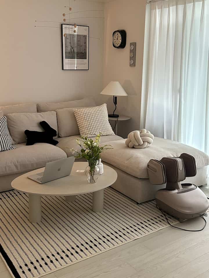 Warm beige-toned living room featuring a beige sectional sofa, striped rug, round coffee table, and a foot massager creating a cozy atmosphere