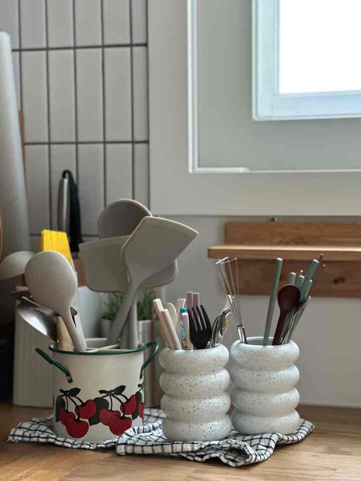 White and wood-toned kitchen featuring vintage utensil containers and various kitchen tools with a neat atmosphere
