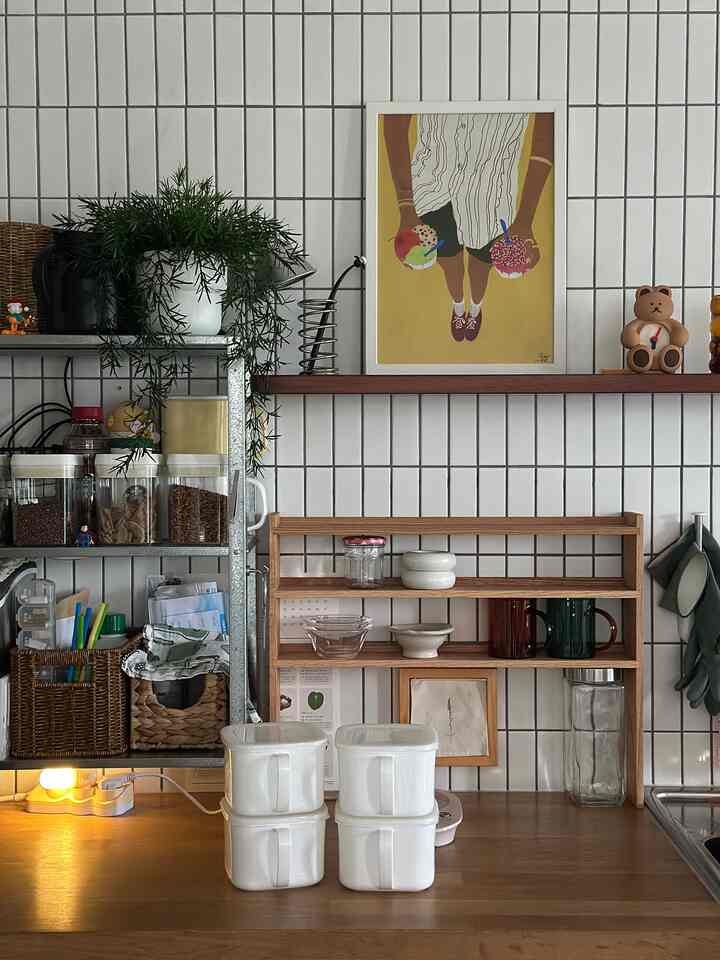 Kitchen space with white tiled walls and wooden shelves, featuring neatly arranged canisters and dishware in a natural tone