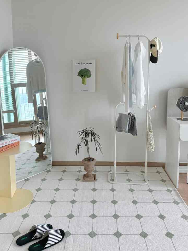 White and green toned walk-in closet featuring a large full-length mirror, side table, and patterned rug in a clean and fresh space