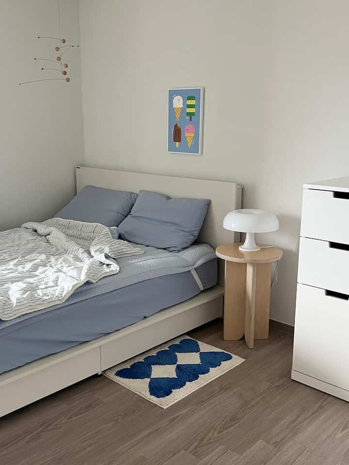 白と青のトーンの寝室、シンプルなベッドとブルーの寝具、爽やかなアイスクリームのポスターが調和した雰囲気のあるインテリア