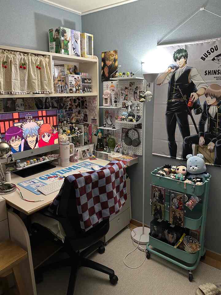 Pastel blue-walled compact home office for a single household, featuring a beige desk and anime character goods creating a cozy atmosphere