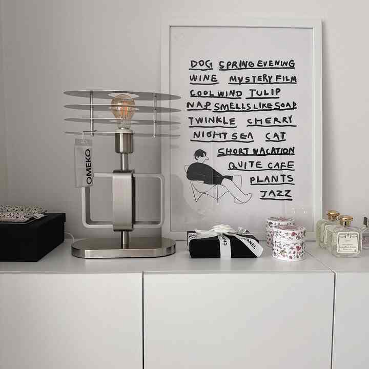 モノトーンと白色調のミニマルなインテリア空間、中央にメタルのテーブルランプとポスターが配置された棚