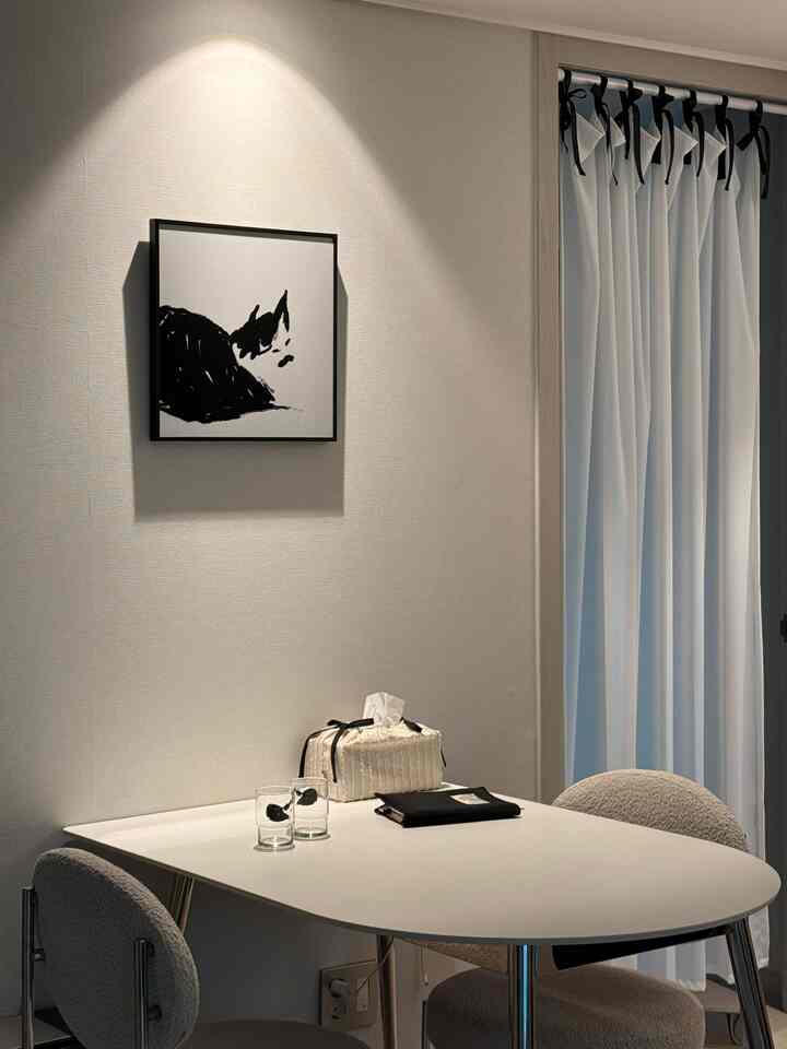 White and black toned living space corner featuring a cat artwork and ribbon-tied curtains in a minimalist style
